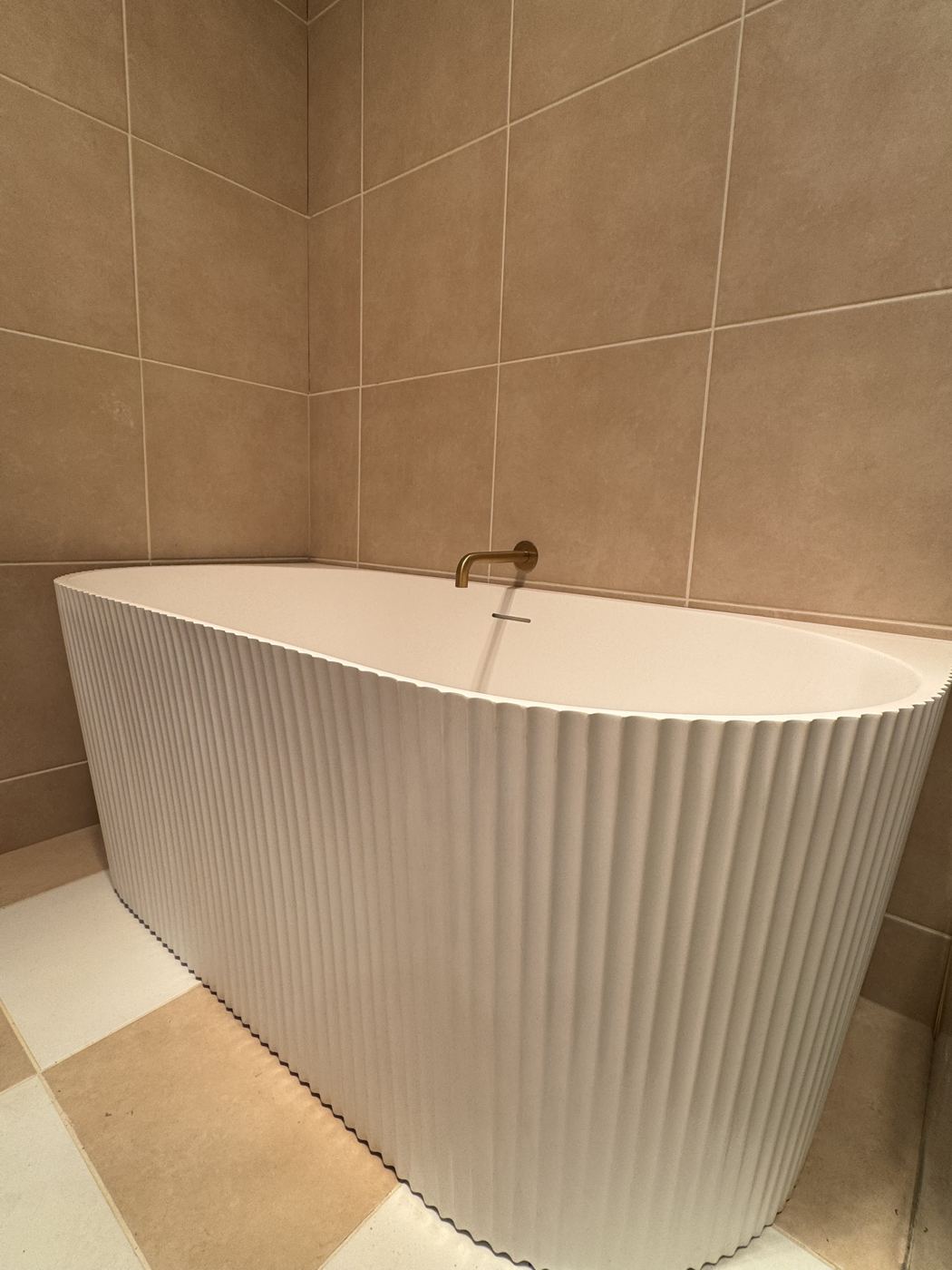 Close view of a fluted white bath with brass spout