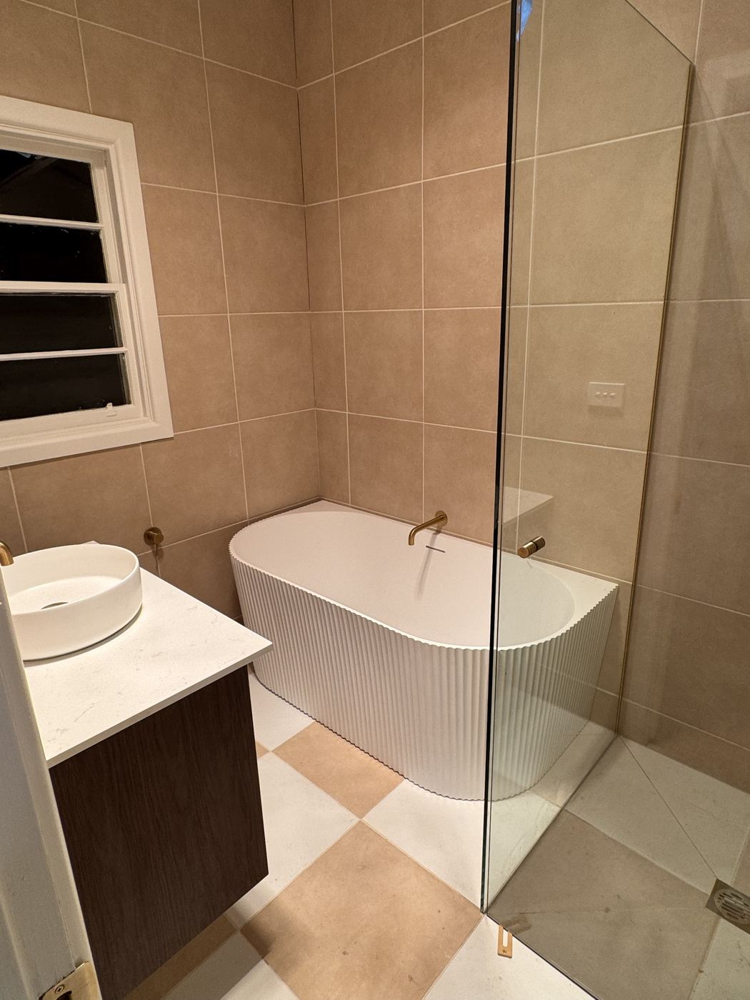 Bathroom with fluted freestanding bath, brushed brass tapware and checkerboard floor
