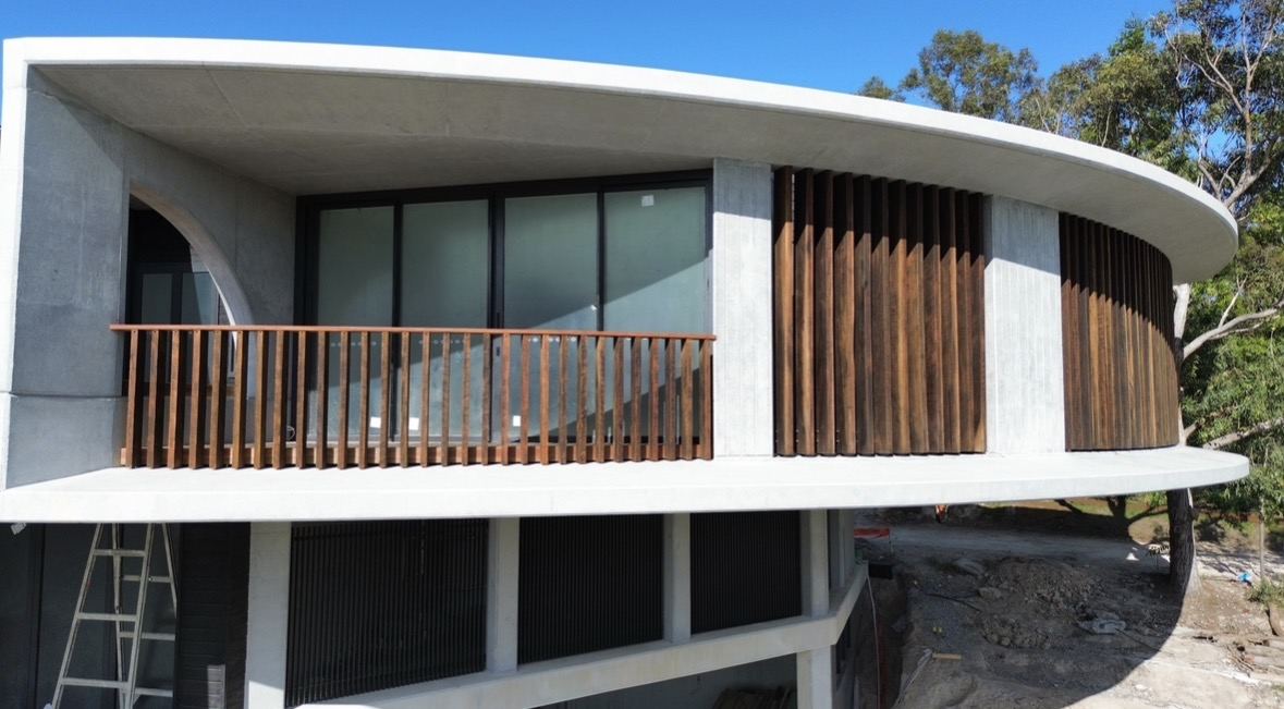 Curved concrete home with hardwood balustrade and vertical hardwood screening battens