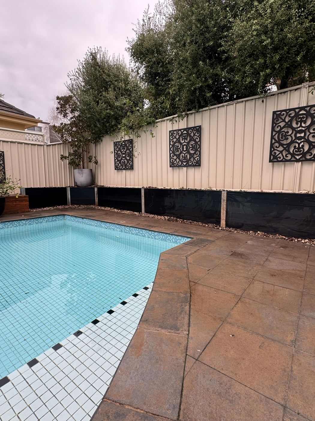Black Ezzy Fit sleeper retaining wall with steel posts beside a pool